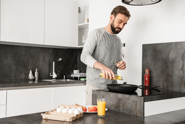 Scapolo bello con capelli corti castani e barba cucinare frittata con verdure in cucina di casa, usando la padella