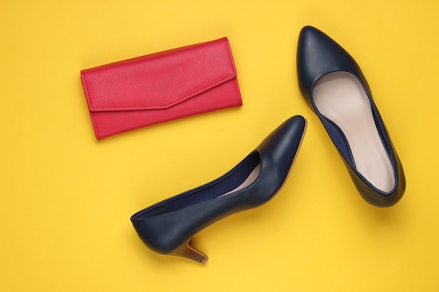 Scarpe classiche con tacco alto, portafoglio in pelle rossa su giallo.