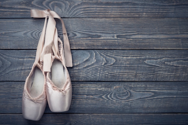 Scarpe da danza classica con un fiocco di nastri appesi a un chiodo su legno