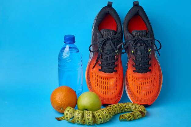 Scarpe da ginnastica arancioni che misurano la bottiglia d'acqua e la frutta mele e arance su sfondo blu