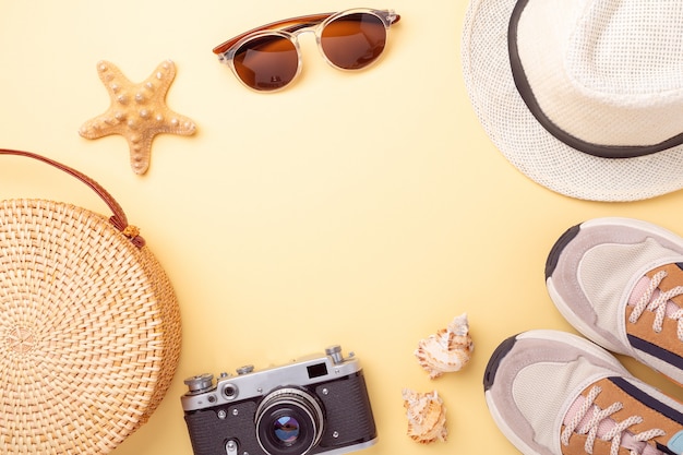 Scarpe da ginnastica, borsa in rattan, occhiali da sole, cappello e fotocamera retrò su uno sfondo giallo. Concetto di viaggio. Disteso