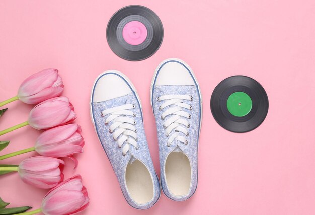 Scarpe da ginnastica e dischi in vinile con bouquet di tulipani rosa su sfondo rosa Giorno della musica Vista dall'alto