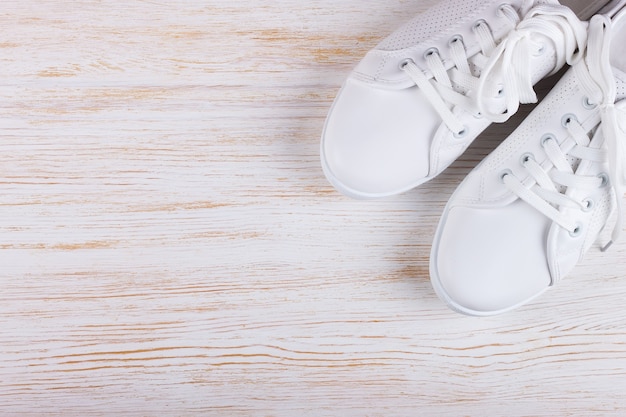 Scarpe da ginnastica femminili bianche su fondo di legno bianco con lo spazio della copia. vista dall'alto, piatto.