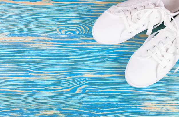 Scarpe da ginnastica femminili bianche su fondo di legno blu con lo spazio della copia. vista dall'alto, piatto.