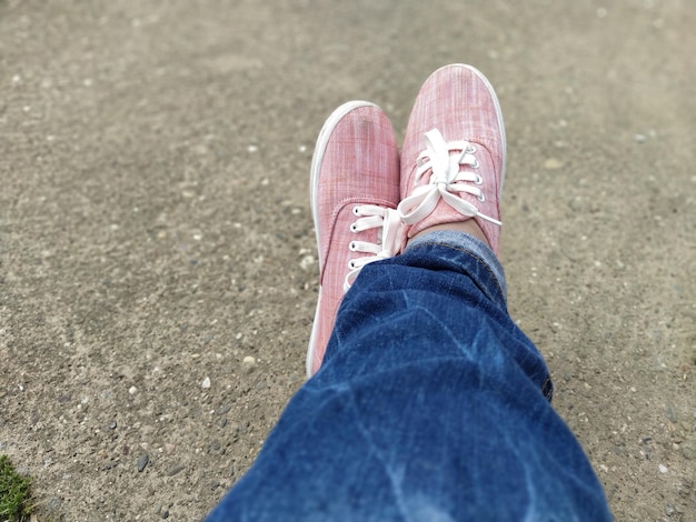 Scarpe da ginnastica rosa con lacci bianchi sulle gambe blue jeans avvolti sotto vista dall'alto spensierata