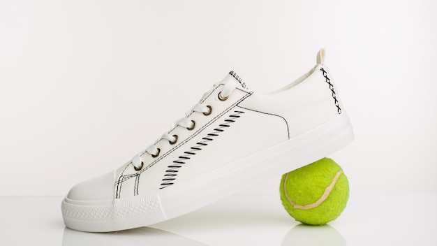 Scarpe da passeggio bianche alla moda con palla da tennis su sfondo bianco. - Immagine