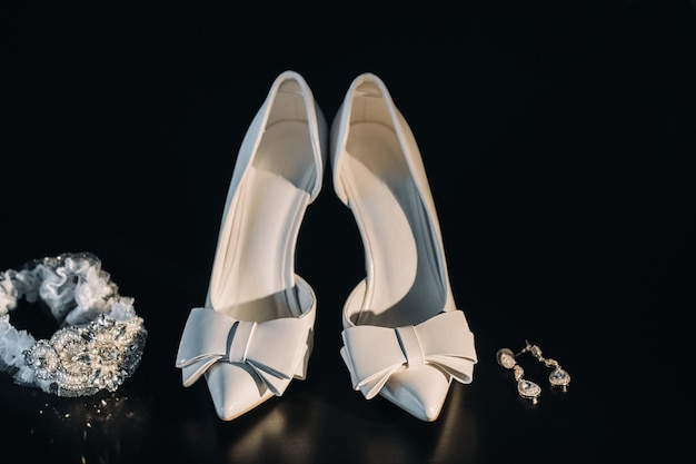 Scarpe da sposa bianche e reggicalze con orecchini su sfondo nero