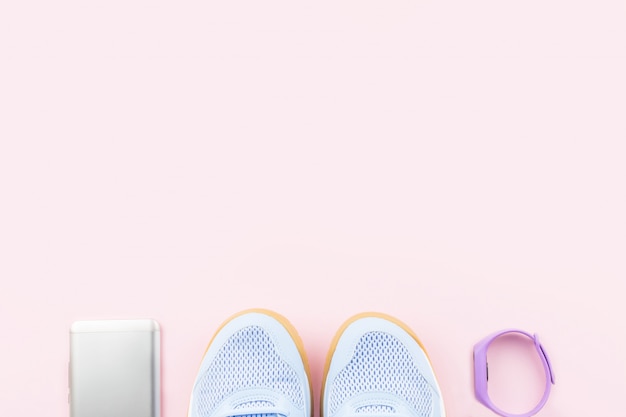 Scarpe da tennis, inseguitore di fitness e smartphone femminili viola su fondo rosa. Disteso, copia spazio.