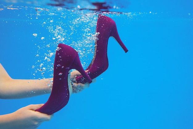 Scarpe di velluto viola nelle mani della donna sott'acqua in piscina su sfondo blu