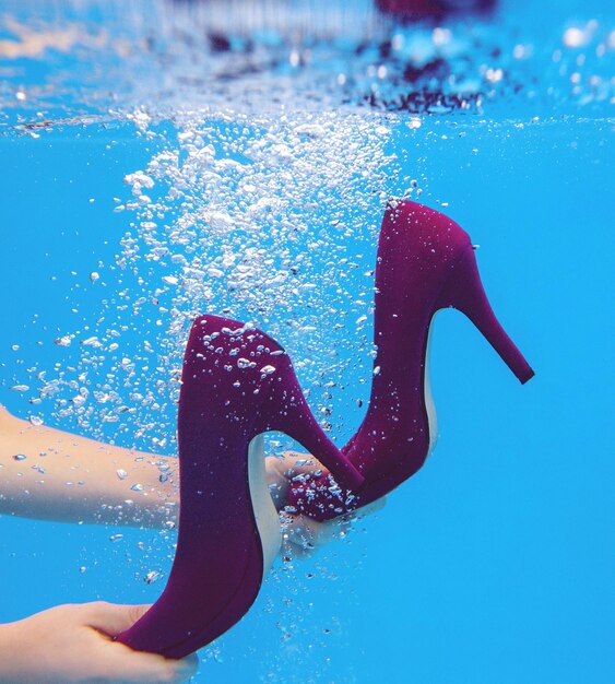 Scarpe di velluto viola nelle mani della donna sott'acqua in piscina su sfondo blu