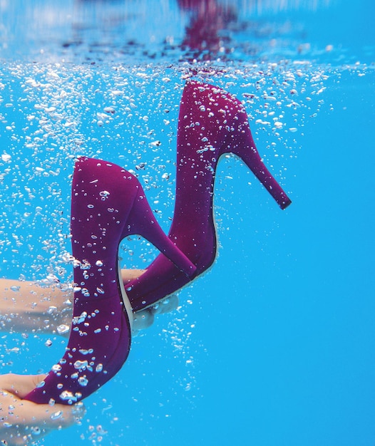 Scarpe di velluto viola nelle mani della donna sott'acqua in piscina su sfondo blu