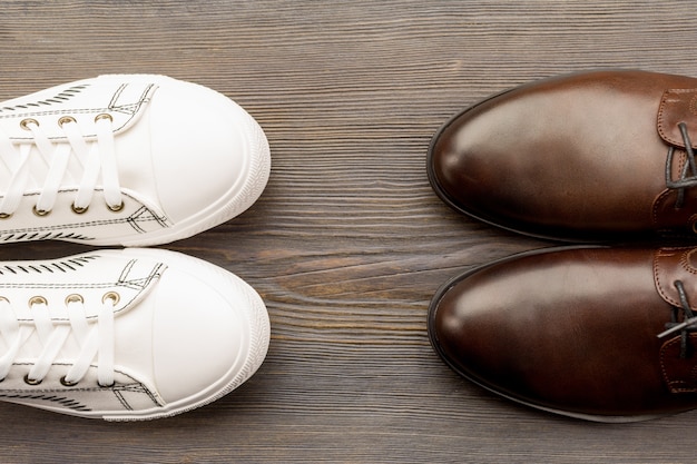 Scarpe marroni classiche da uomo e scarpe da ginnastica bianche su un legno