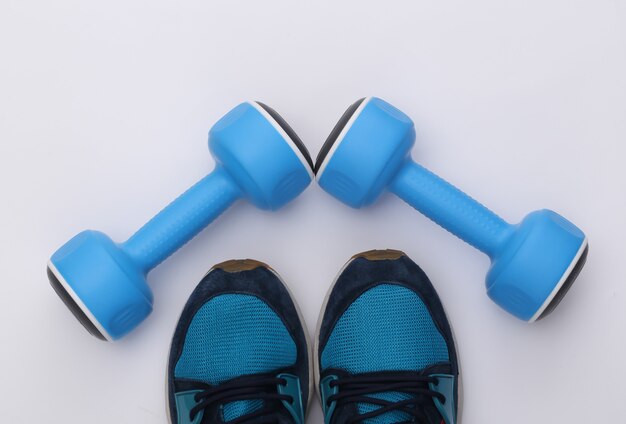 Scarpe sportive (scarpe da ginnastica) e manubri blu su sfondo bianco. Stile di vita sano, allenamento fitness. Vista dall'alto