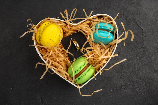 scatola a forma di cuore vista dall'alto con anello di fidanzamento macarons su sfondo scuro