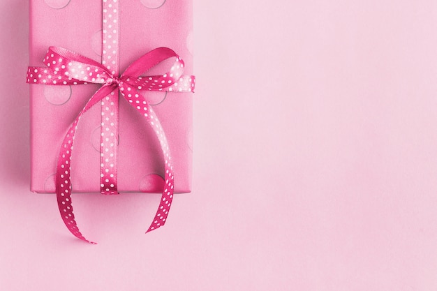 Scatola avvolta in carta regalo rosa e nastro, su uno sfondo rosa