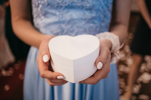 Scatola bianca a forma di cuore con diamante nelle mani della ragazza in blu dresd