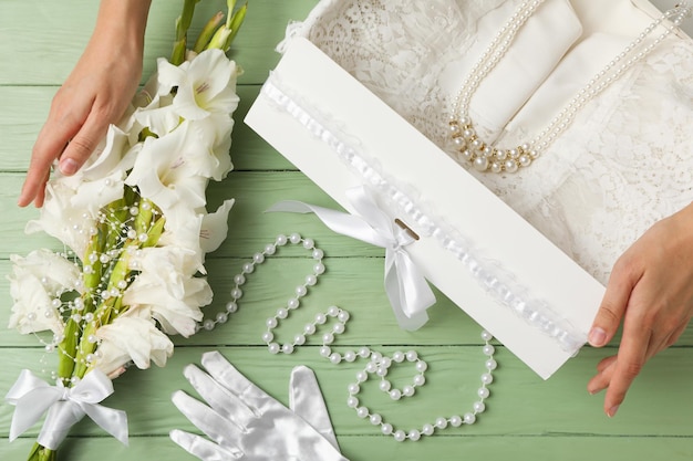 Scatola con fiori di gioielli abito da sposa e mani femminili su sfondo verde vista dall'alto