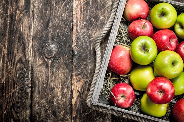 Scatola con mele rosse e verdi fresche. Su uno sfondo di legno.