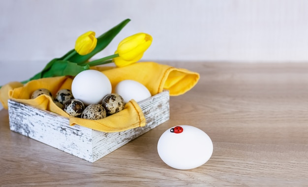 Scatola con uova di Pasqua e tulipani gialli su un tavolo di legno