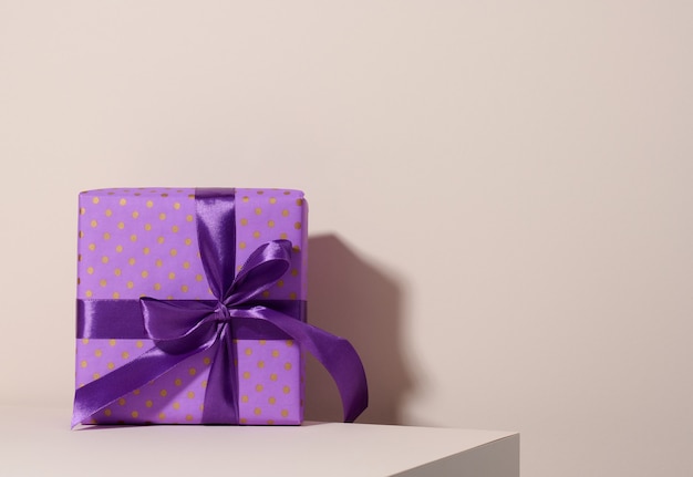 Scatola confezionata in carta viola festiva e legata con nastro di seta su fondo beige, regalo di compleanno, sorpresa