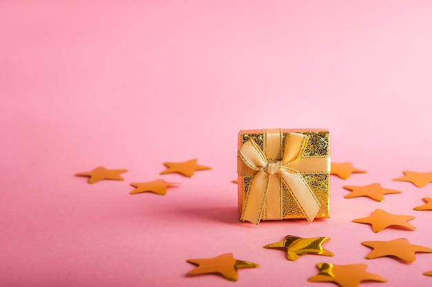 Scatola d'oro con un regalo. Coriandoli di stelle d'oro.