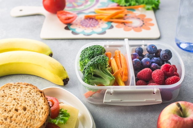 Scatola della refezione con la banana delle bacche delle verdure sulla tavola grigia sana