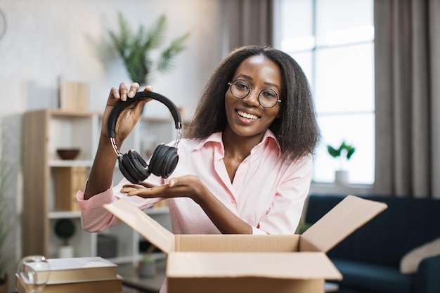 Scatola di apertura sorridente della donna africana con le nuove cuffie