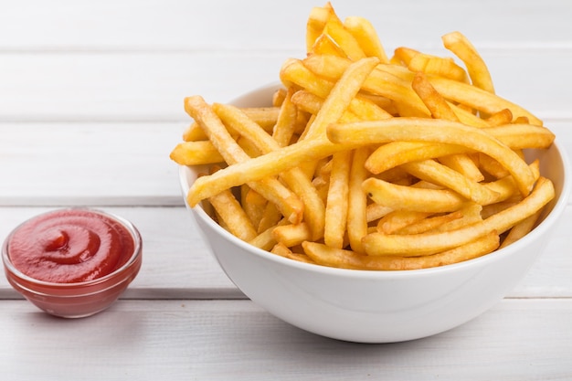 Scatola di carta con una pila di patatine fritte appetitose su sfondo di assi bianche