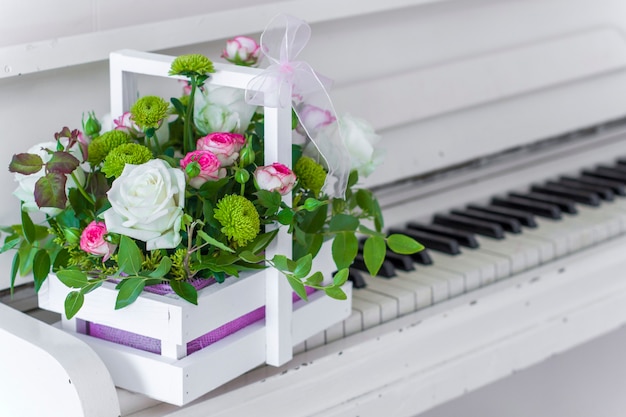 Scatola di legno bianca con bouquet di rose bianche e rosa e crisantemi sul pianoforte bianco. Decorazione della casa. Scatole di fiori. Decorazione di nozze