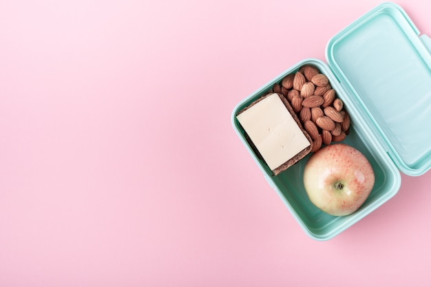 Scatola di pranzo con mela, panino e mandorla sul rosa