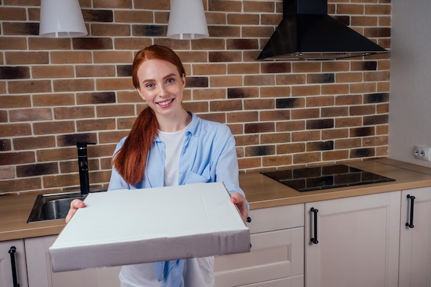 Scatola femminile dai capelli rossi con pizza in cucina a casa