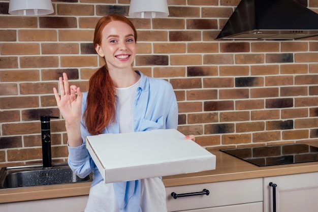 Scatola femminile dai capelli rossi con pizza in cucina a casa