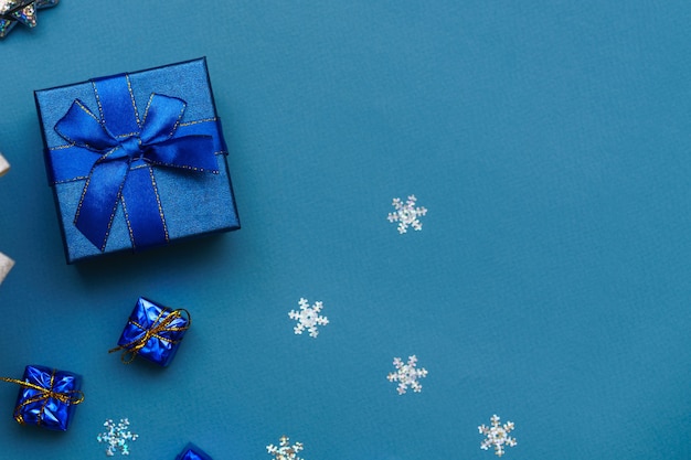 Scatola festiva da vicino fiocco blu su sfondo blu con palle di natale e fiocchi di neve capodanno cristo...