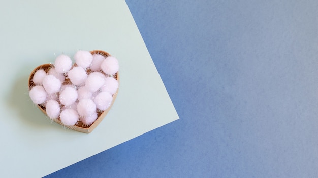 Scatola regalo a forma di cuore con fiocchi di neve decorativi soffici bianchi su sfondo blu bicolore.