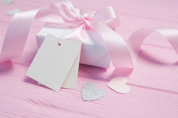 Scatola regalo bianca con fiocco in raso rosa e nastro su fondo in legno rosa. Cartolina di San Valentino