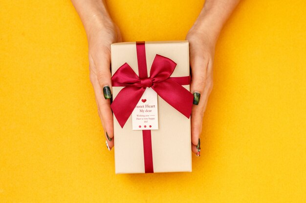 Scatola regalo biodegradabile in cartone nelle mani delle donne su giallo