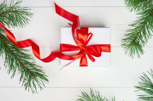 Scatola regalo di Natale con nastro rosso e rami di pino su bianco