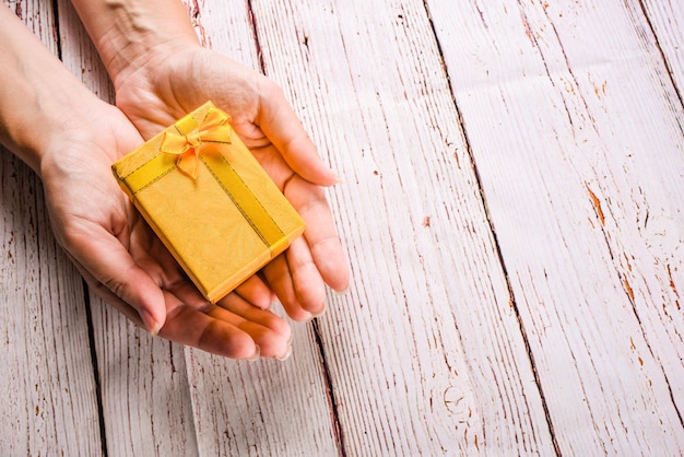 scatola regalo gialla con nastro di prua nelle mani di donna sullo spazio di legno bianco