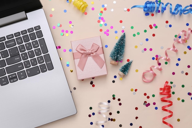 Scatola regalo per mini alberi di Natale per laptop e serpentina colorata con coriandoli su sfondo beige Sfondo natalizio