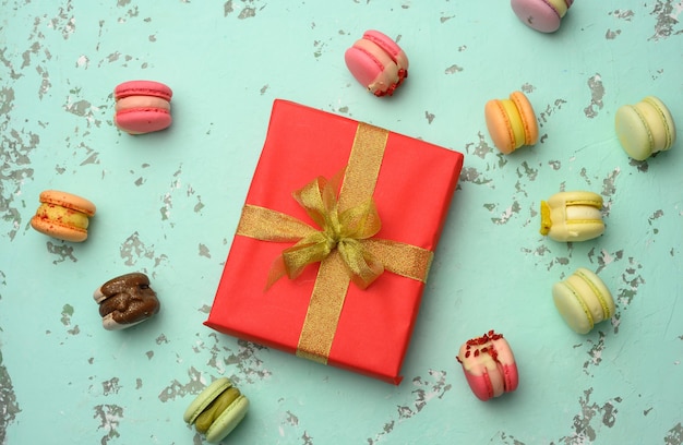 Scatola regalo quadrata rossa con fiocco e macarons al forno su sfondo verde, vista dall'alto