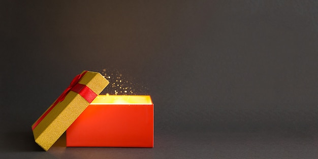 Scatola regalo rossa aperta con un fiocco con un bagliore dorato e glitter all'interno su un nero