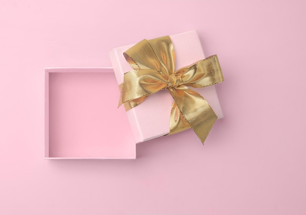 Scatola regalo vuota rosa aperta con fiocco dorato dorato e nastro