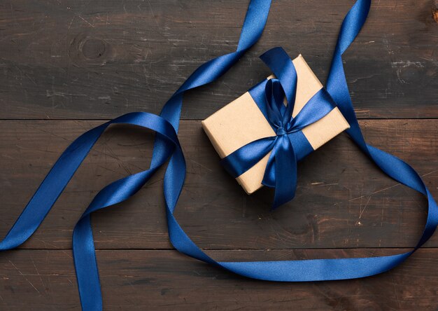 Scatola rettangolare avvolta in carta marrone e legata con un nastro di seta blu con fiocco, regalo su fondo di legno marrone, vista dall'alto