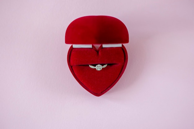 Scatola rossa a forma di cuore con anello di fidanzamento su sfondo rosa