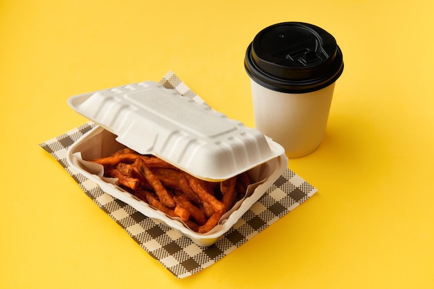 Scatole per il pranzo con patatine fritte, bevanda e salsa di patate dolci su tavolo giallo Piatto piano vista dall'alto concetto di consegna del cibo