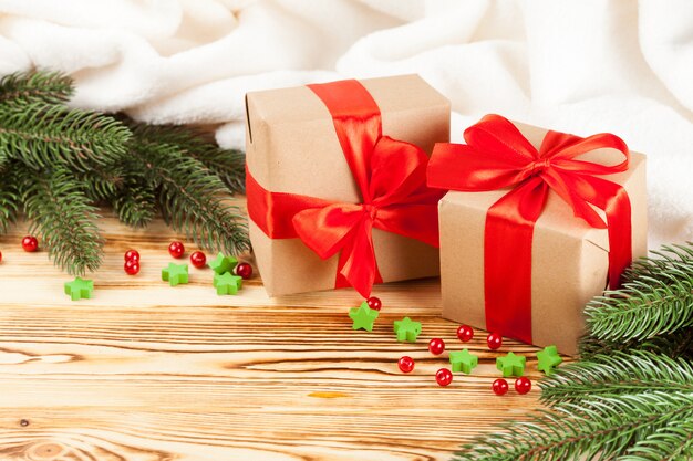 Scatole regalo artigianale con nastro rosso, fiocco, albero di Natale verde, decorazioni su fondo in legno.