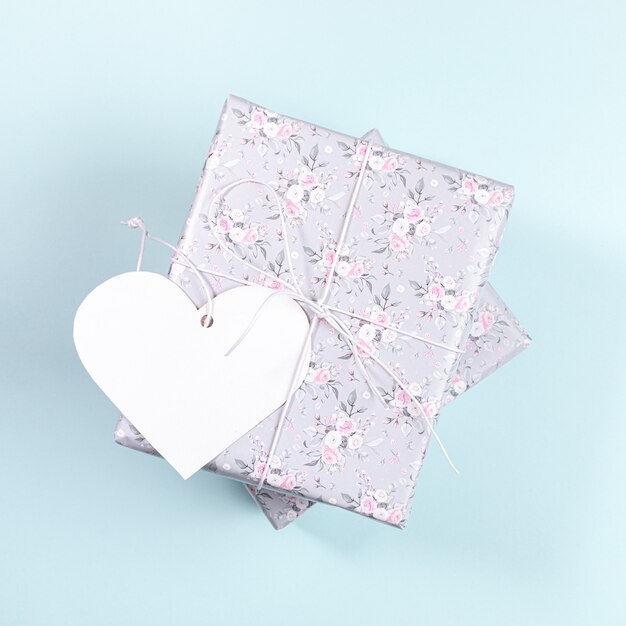 Scatole regalo avvolte con carta grigia con disegno floreale e cuore di carta bianco su azzurro. San Valentino.