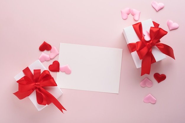 Scatole regalo bianche con nastro rosso e piccoli cuori decorativi rossi su sfondo rosa. Vista dall'alto con spazio di copia. Concetto romantico di San Valentino o matrimonio. Composizione festiva. Modello.