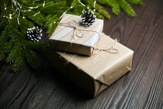 Scatole regalo con luce di Natale e ramo di albero con coni su fondo di legno marrone