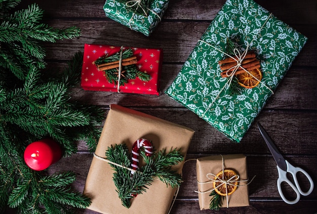 Scatole regalo di Natale con decorazioni in carta kraft, rossa e verde, forbici, candele e rami di pino